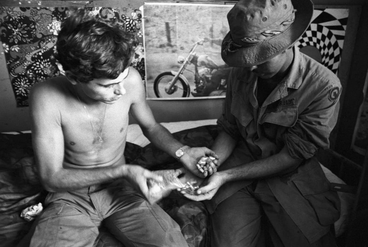 <b>La Guerra de Vietnam y la ‘Guerra contra las Drogas’. </b>El largo conflicto entre Estados Unidos y Vietnam aumentó el contrabando de heroína a los Estados Unidos. En 1971 dos congresistas viajaron al país asiático y descubrieron que alrededor de 
<a href="https://www.michaelshouse.com/blog/what-we-can-learn-from-the-vietnam-war-and-heroin-addiction/"><u>15% de los soldados activos eran adictos a la heroína</u></a>, y muchos consumían otras drogas. El número de personas dependientes de la heroína en los Estados Unidos se disparó a 750,000 durante estos años.
<br>
<br>En 1970 se aprobó la Ley de Prevención y Control Integral del Abuso de Drogas, en 1971 el presidente Nixon declaró una "guerra contra las drogas" y en 1973 fue fundada la 
<a href="https://www.dea.gov/history"><u>Administración para el Control de Drogas</u></a>, DEA, por sus siglas en inglés. La fotografía muestra un intercambio de heroína entre soldados estadounidenses durante la guerra de Vietnam.