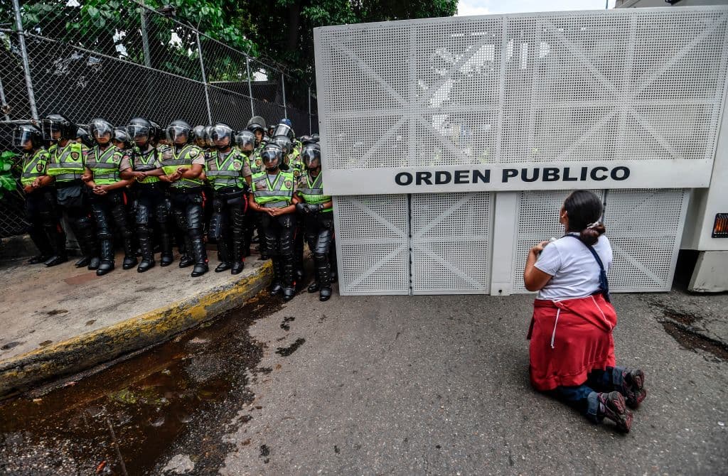 Una mujer se arrodilla frente a un cordón de la Policía Nacional Bolivariana que intentó frenar la llegada de una de las marchas opositoras a su destino final, la Conferencia Episcopal Venezolana, este sábado. Uno de los grupos que caminaba desde el este de la ciudad fue bloqueado por la militar Guardia Nacional, pero los manifestantes negociaron con los agentes y, al final, les permitieron el paso. (Juan Barreto/AFP/GettyImages)