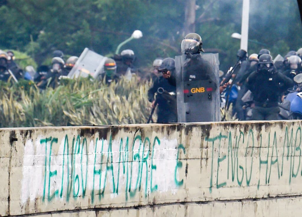 Otra fotografía del mismo encuentro entre Guardia nacional y opositores, difundida por la agencia France-Presse, muestra a un funcionario de la Guardia Nacional enmascarasdo que lleva un escudo del equipo antimotines y una pistola en su mano derecha.