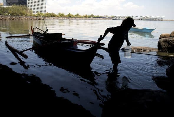 Un pescador jala su barco bajo un puente en Manila.