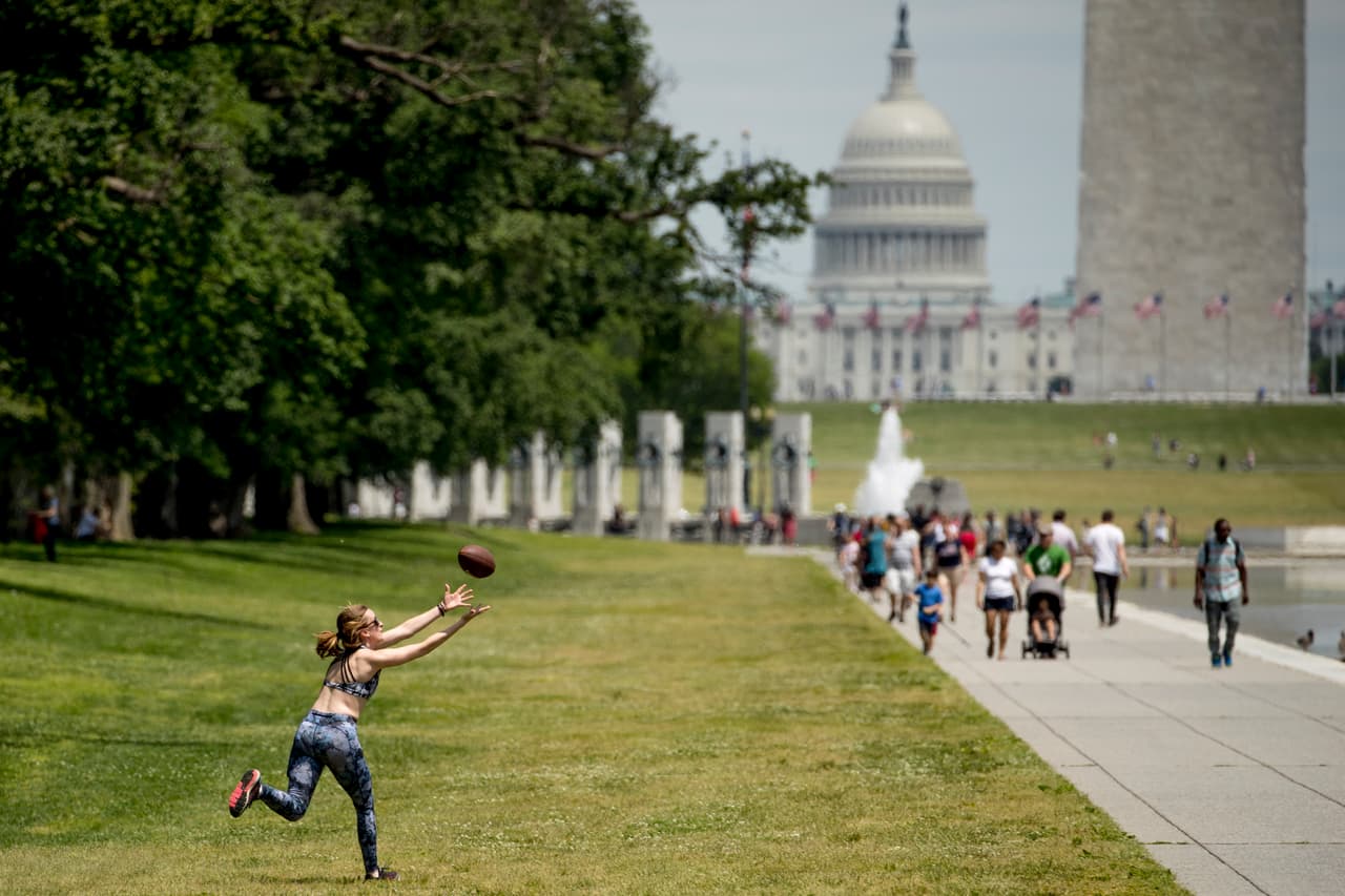 La cúpula del Capitolio de los EE. UU. Y el Monumento a Washington son visibles cuando una mujer atrapa un balón de fútbol a lo largo de las orillas de la Piscina reflectante en el National Mall en Washington.
