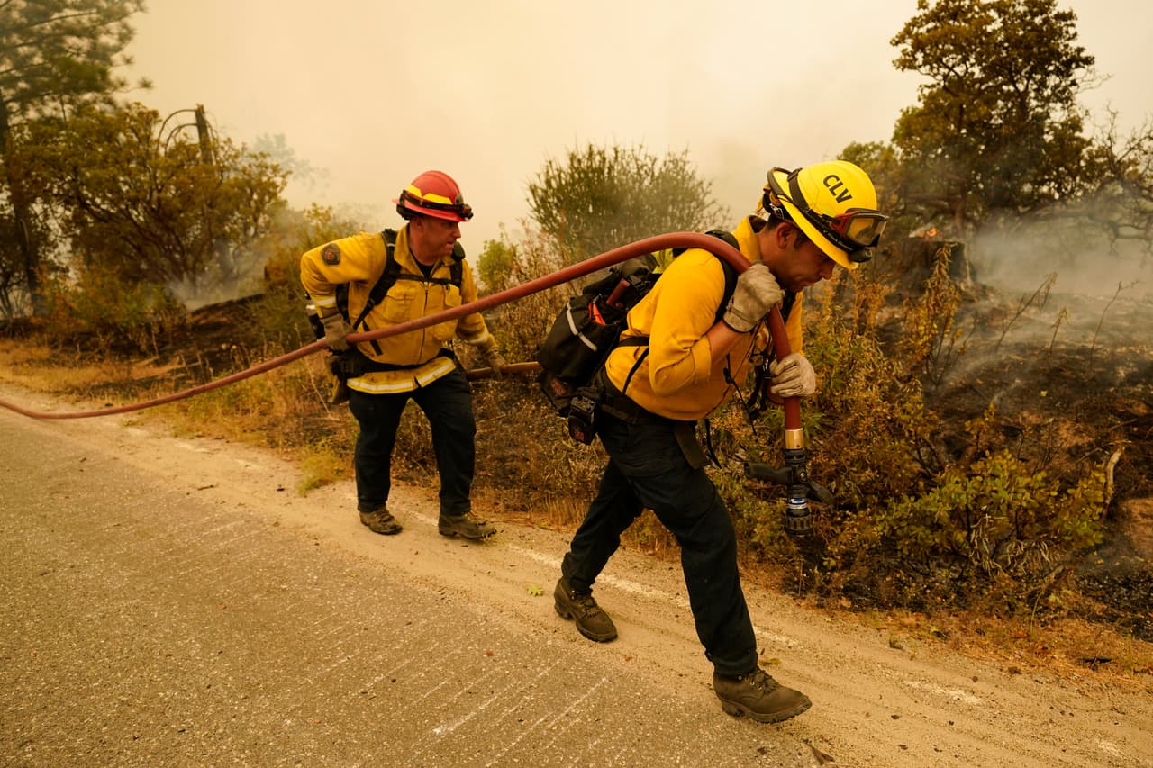 Tim Lesmeister -izquierda- y Rick Archuleta, del Departamento de Bomberos de Clovis, caminan a lo largo de una carretera que monitorea los puntos calientes que dejó el incendio de Creek en Tollhouse, California.
<br>