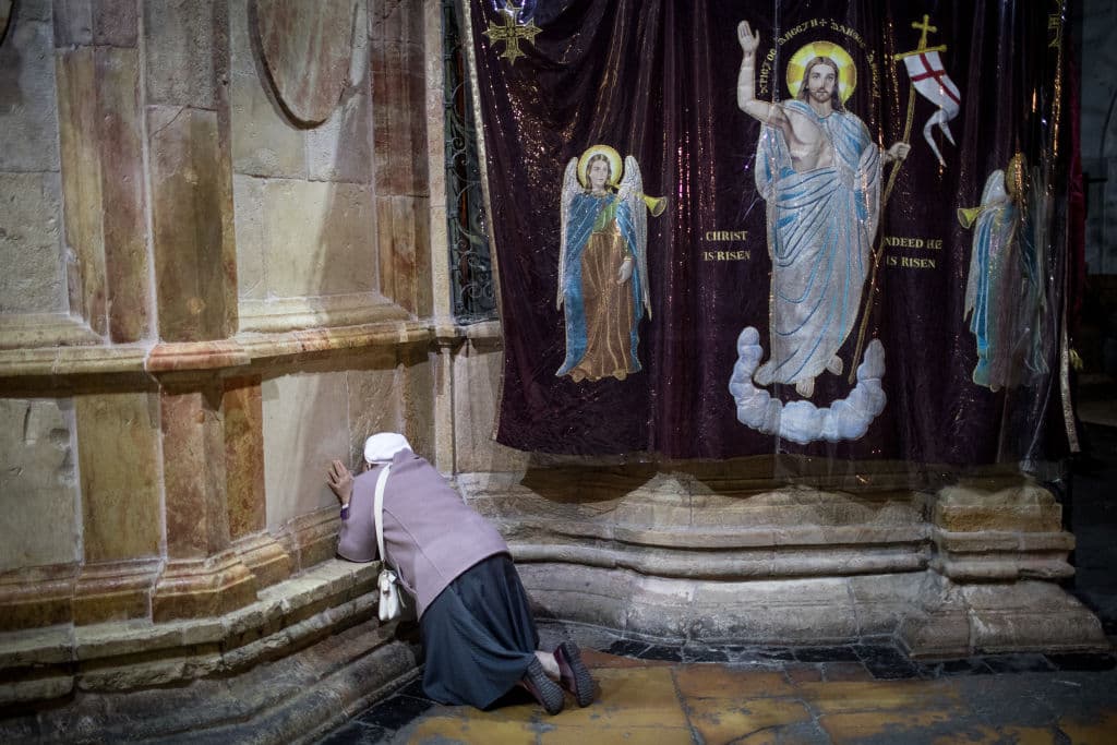 Una mujer reza hincada sobre la tumba de Jesucristo en Jerusalén, tras la procesión y misa de Jueves Santo.