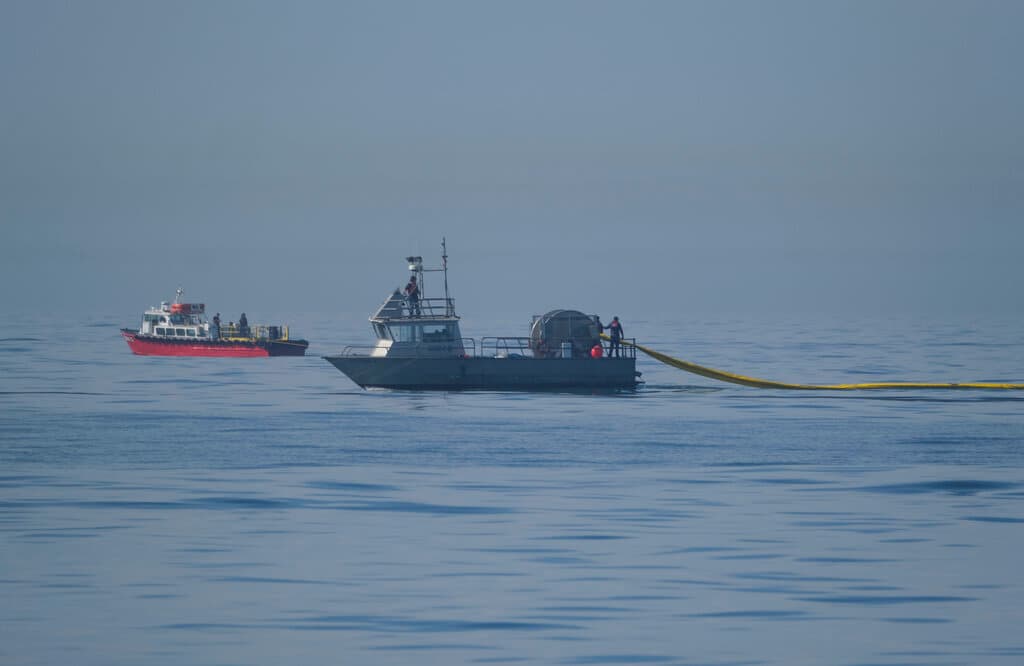 Una embarcación de la Marine Spill Response Corporation (MSRC), en primer plano, una organización que se dedica a eliminar derrames de petróleo (OSRO), despliega barreras flotantes conocidas como barreras para tratar de detener la incursión de una mancha de hidrocarburo frente a Huntington Beach, California, el domingo 3 de octubre de 2021.