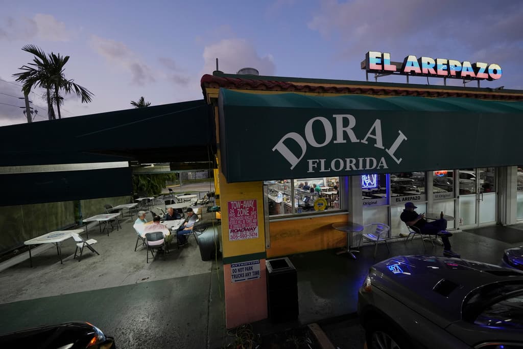 Ciudadanos estadounidenses que inmigraron de Venezuela hace entre 16 y 30 años juegan al dominó fuera de El Arepazo, un restaurante que es un punto de encuentro de la comunidad venezolana en Estados Unidos, en Doral, Florida, el miércoles 2 de abril de 2025. Muchos de los amigos, como César Mena, a la derecha, votaron por el presidente Donald Trump y le siguen apoyando. Mena dijo que tenía familiares y amigos amparados por el TPS, y lo lamentaba por ellos, pero era una situación temporal y había un problema que resolver. (AP Foto/Rebecca Blackwell)