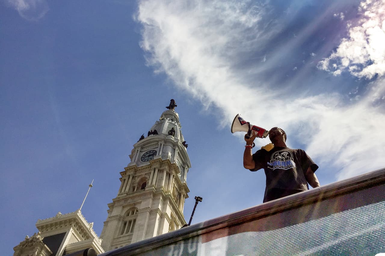 DOMINGO 24 DE JULIO. 3:13 PM. La tarde del domingo. Todavía falta un día para que empiece la convención nacional del partido demócrata. En el centro de Filadelfia, frente al City Hall, partidarios de Bernie Sanders se reúnen para manifestar. Un miembro del grupo "Black men for Bernie" toma la palabra ante los cientos de asistentes.