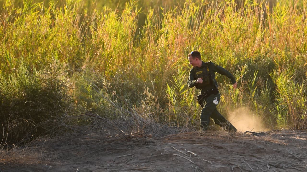 Un agente de la Patrulla Fronteriza busca a alguien que cruza el río Colorado hacia EEUU en el muro fronterizo.