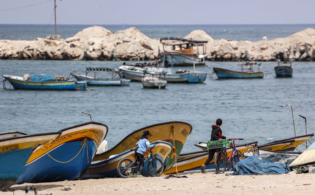 Palestinian boys walk with bicycles past shored fishing boats at the seaport of Gaza City on April 26, 2021.