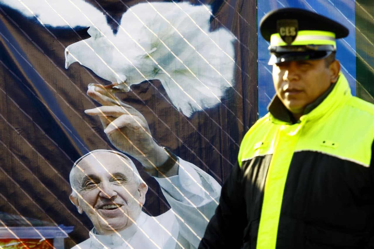 Un miembro de seguridad pasa por un cartel de Francisco en Ecatepec. El pontífice tiene una paloma, que representa al Espíritu Santo, sobre su mano.