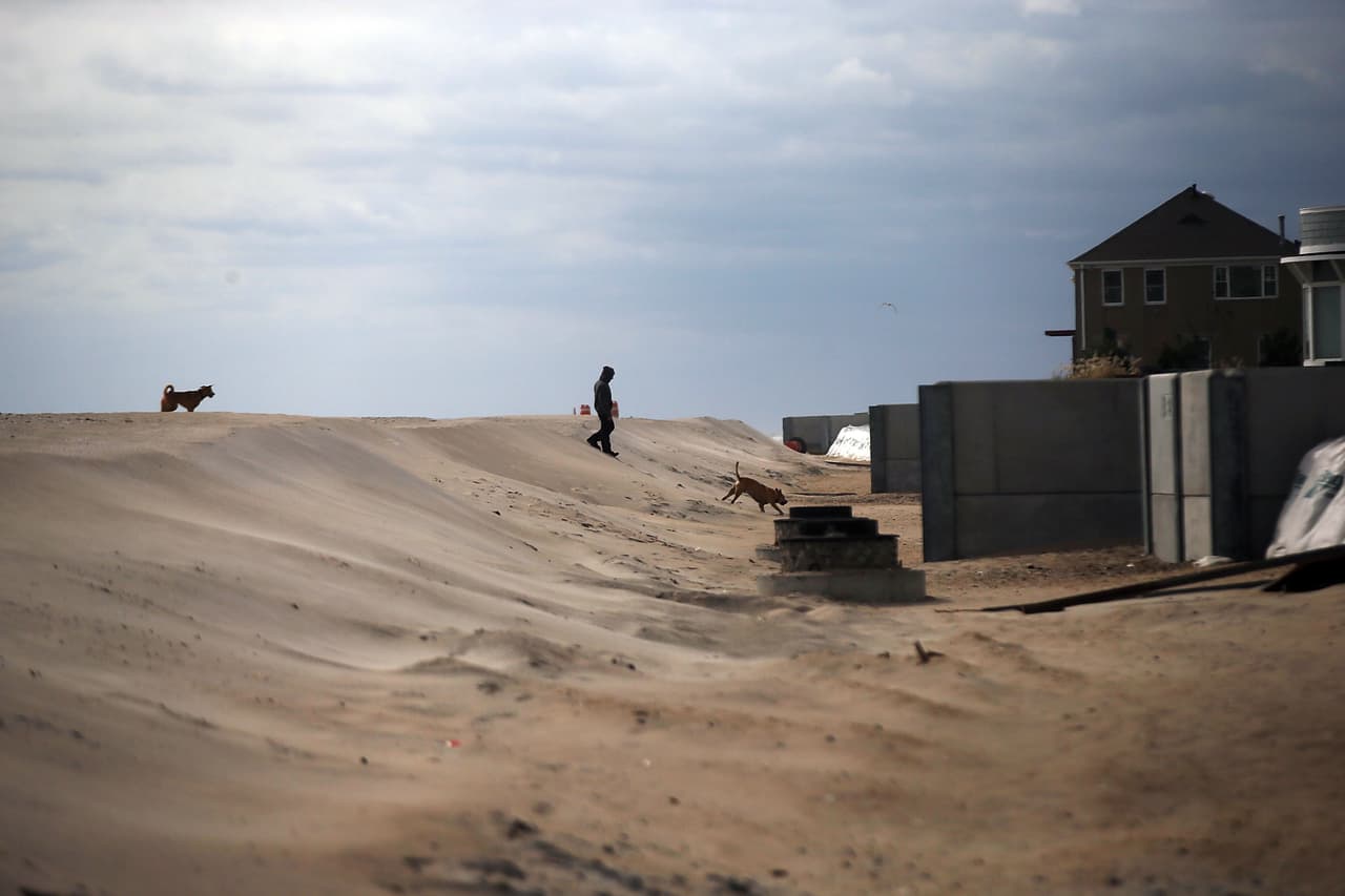 NEW YORK, NY - OCTOBER 09: A man walks with his dog along newly built protective sand berms in front of beachfront property on October 9, 2013 in the Belle Harbor neighborhood, in the Queens borough of New York City. Nearly one year after Hurricane Sandy devastated much of the area with severe flooding and wind damage, the Rockaways and Belle Harbor have made great headway with rebuilding and renovations to the iconic beach community. Despite the progress, the community is still reeling from the destruction of the world famous boardwalk and the closure of many area businesses. Hurricane Sandy made landfall on October 29 near Brigantine, New Jersey and affected 24 states from Florida to Maine and cost the country an estimated $65 billion. (Photo by Spencer Platt/Getty Images)