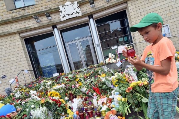 Un niño deposita una vela junto a los arreglos florales.