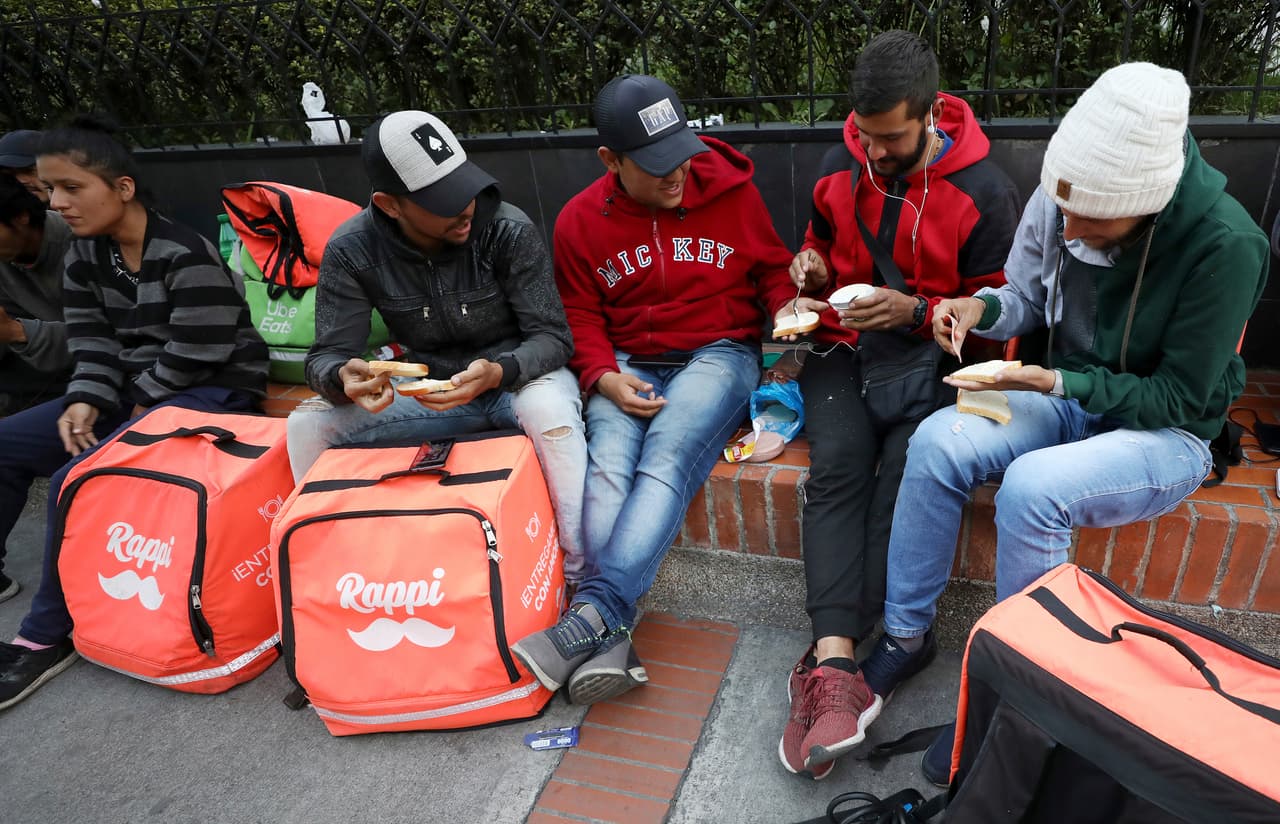 Pero estas innovadoras fuentes de trabajo requieren muchas horas en ocupaciones que dan un pago modesto, sin beneficios y pocas oportunidades para el avance profesional. En Colombia,
<a href="https://www.univision.com/noticias/crisis-en-venezuela/el-exodo-de-venezolanos-sigue-en-aumento-ya-hay-3-millones-de-migrantes-y-refugiados-segun-la-onu">que recientemente ha acogido a más de 1.3 millones de venezolanos que huyen de las dificultades económicas</a>, miles de inmigrantes están trabajando en la plataforma
<i>Rappi</i> y algunos de ellos son profesionales universitarios. En la fotografía un grupo de venezolanos comparten emparedados mientras esperan por nuevas entregas.