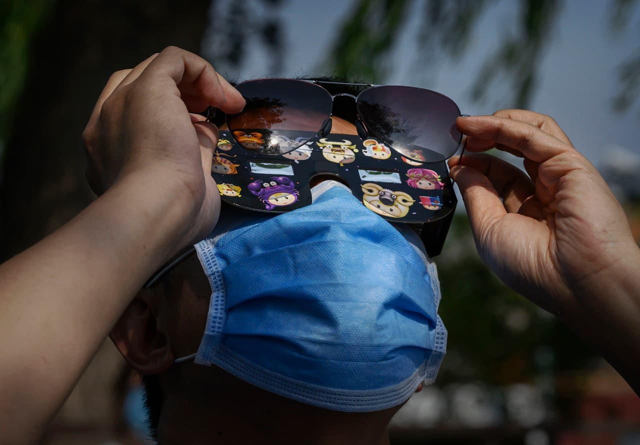 Un hombre chino lleva una máscara protectora para evitar el coronavirus y lentes protectores mientras observa el sol durante el eclipse anular fuera de la Ciudad Prohibida, en Pekín, China.