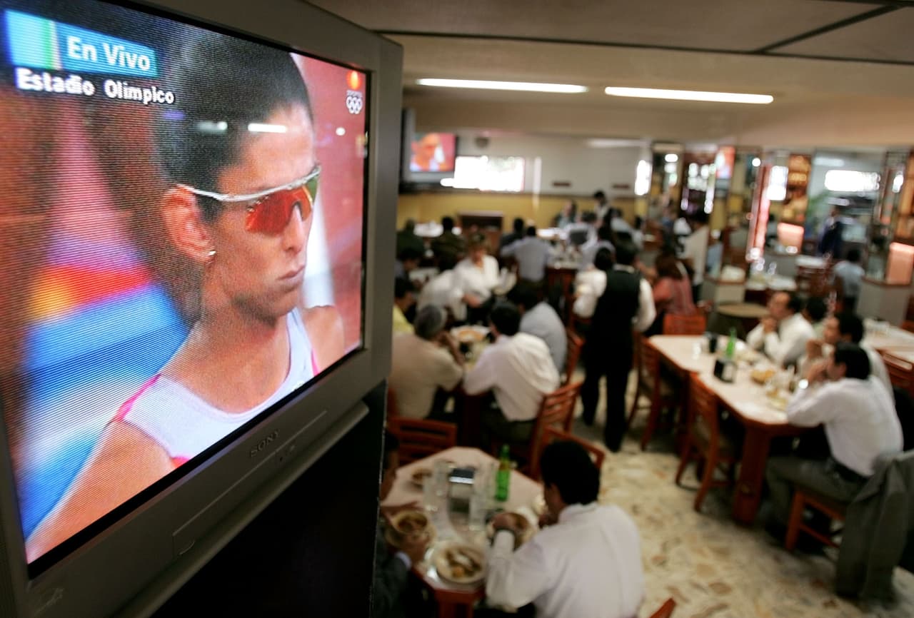 Los asistentes a un restaurante de Ciudad de México miran por televisión a Ana Gabriela Guevara en su participación en la final de los 400 metros planos de los Juegos Olímpicos de Atenas, donde obtuvo la medalla de plata.