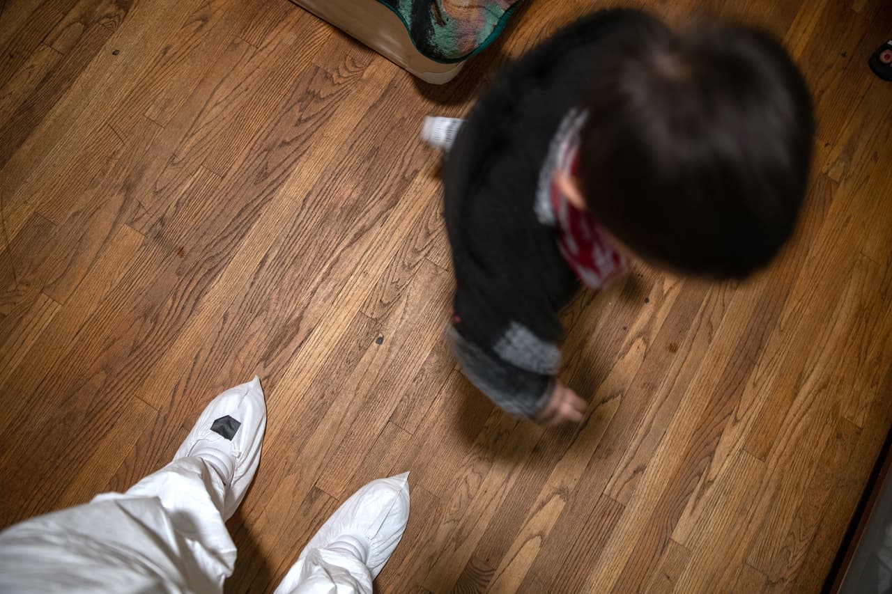 El pequeño inmigrante juega junto a las piernas del autor de estas fotografías, protegido del contagio del coronavirus con un traje sintético.