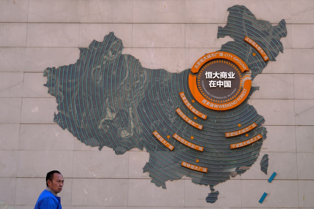 Una persona pasa enfrente de un muro en Pekín, China, que muestra un mapa del país asiático con los complejos inmobiliarios en desarrollo de Evergrande.