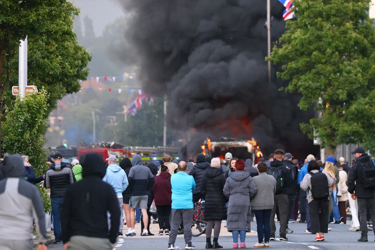 Unas personas observan cómo arde un vehículo durante una protesta. Foto AP/Peter Morrison)