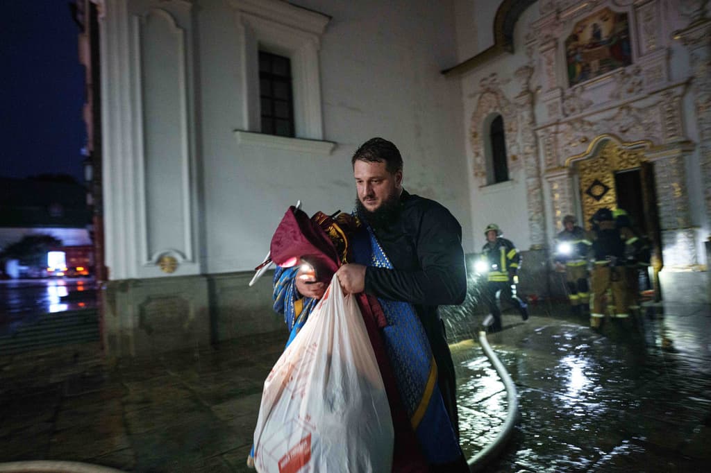 Un sacerdote saca objetos de la iglesia de la catedral de la Dormición de la Lavra de Kiev-Pechersk, también conocida como el Monasterio de las Cuevas, mientras arde tras un ataque ruso contra Kiev, Ucrania, el lunes 15 de junio de 2026. (Foto AP/Evgeniy Maloletka)