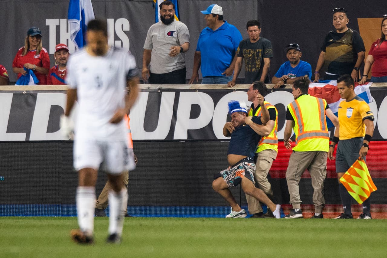 Un espectador que se lanzó al campo de juego es detenido por miembros de la seguridad del estadio.
