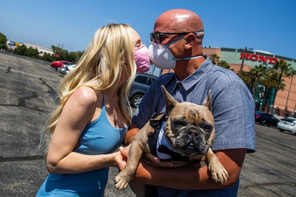 <b>Un testigo peludo. </b>Chad Robbins y Tracey Robbins (der.) se besan por sobre las mascarillas faciales mientras sostienen a su perro Huggy después de la ceremonia de su boda en Anaheim. Las bodas no puden reunir a mucha gente debido a la crisis del coronavirus que según el conteo más reciente de Univision ha costado la vida de 1,440 personas en California y 843,981en los Estados Unidos.