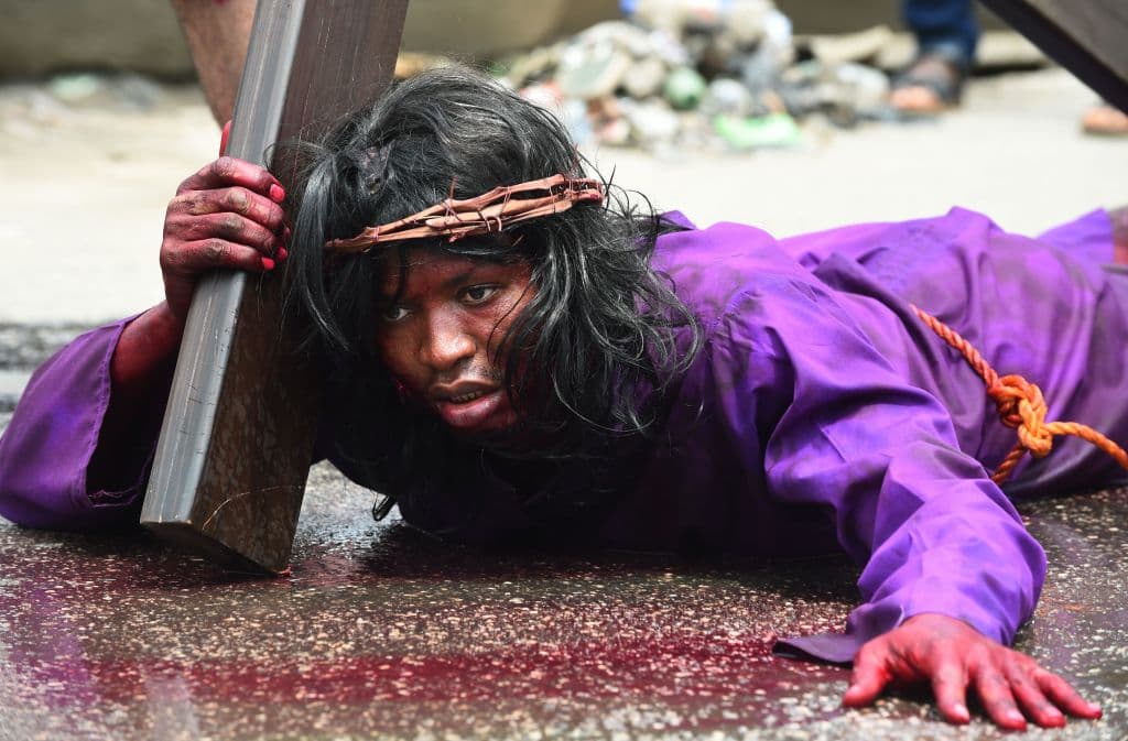 En Nigeria, un actor que representa a Jesucristo se rinde ante el peso de la cruz y se deja caer en su actuación del Vía Crucis.