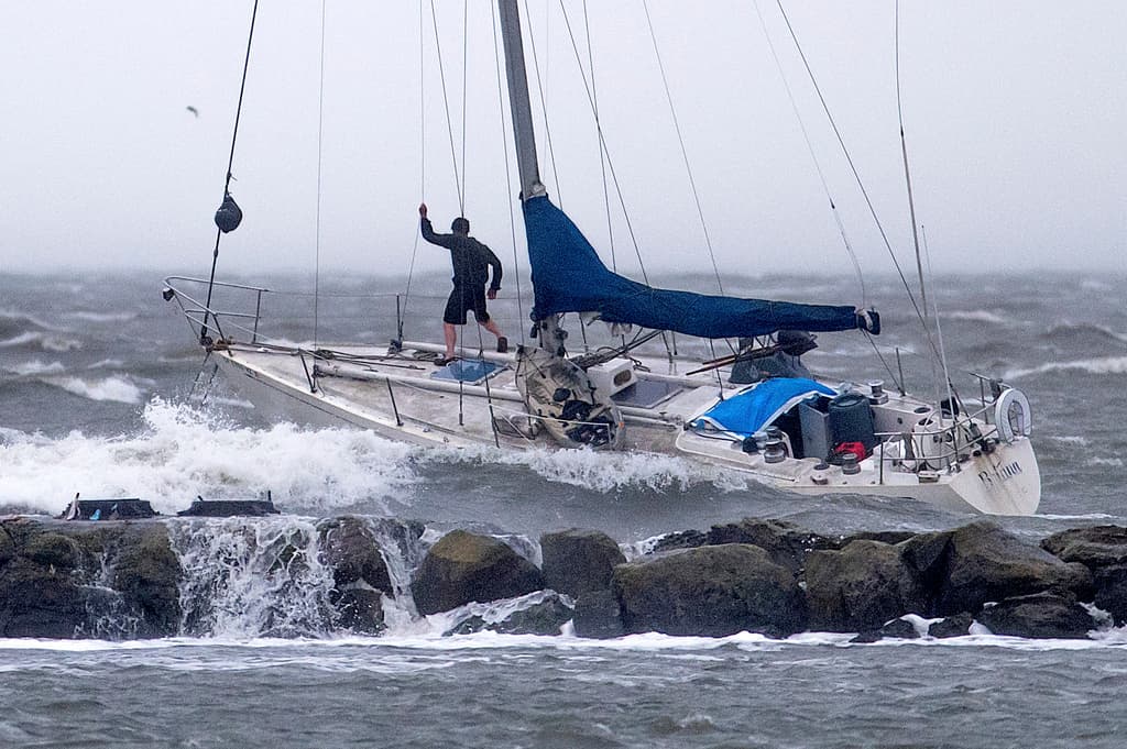 Un navegante se encuentra en la proa de un velero anclado mientras las olas rompen sobre un rompeolas en Alameda, California, el domingo 4 de febrero de 2024, en Alameda, California. Fuertes vientos y fuertes lluvias están afectando la región. (Foto AP/Noah Berger)