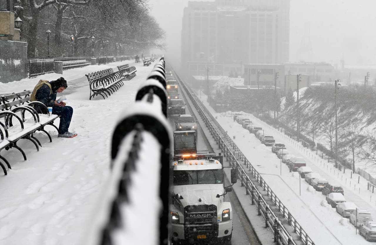 Un hombre sentado en un banco durante una nevada en el paseo de Brooklyn