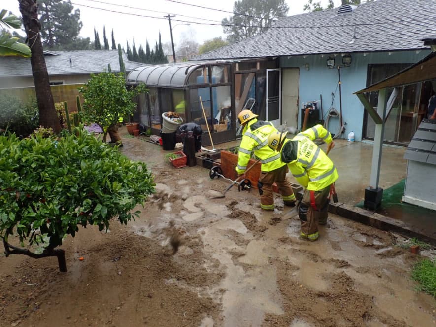 Bomberos abren zanjas para redirigir el agua y lodo que baja de los cerros.