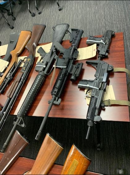 Con la ayuda de la policía de Menifee, agentes del Departamento de Justicia de California acudieron a la casa con una orden de allanamiento y recuperaron 54 armas, incluidos dos rifles de asalto AR-15, dos armas de asalto UZI, 35 pistolas, 157 cargadores y 2,200 rondas de municiones.
<br>
<br>Tres de las armas estaban cargadas, ubicadas a la vista y no guardadas en una caja fuerte que sería inaccesible para la persona prohibida.
<br>