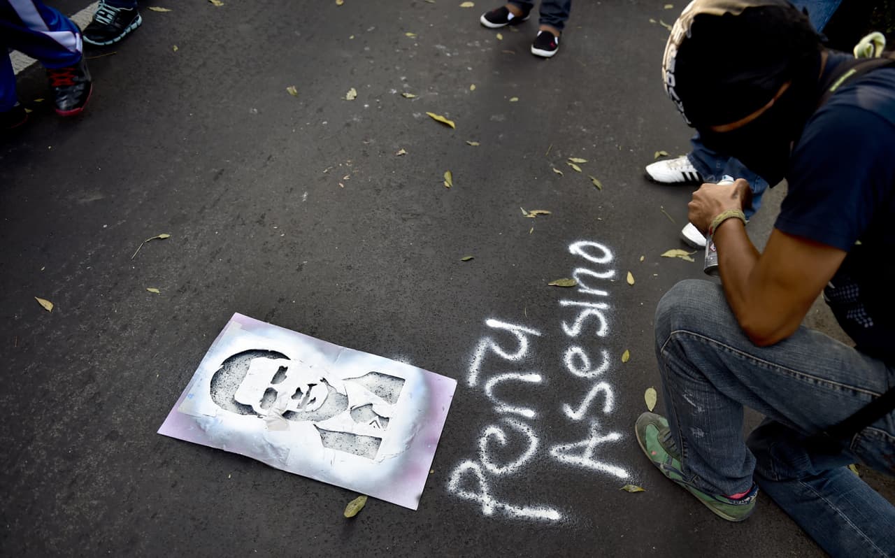 Un manifestante enmascarado utiliza un molde de esténcil para hacer un grafiti con la imagen del presidente mejicano Enrique Peña Nieto, en ciudad de México.