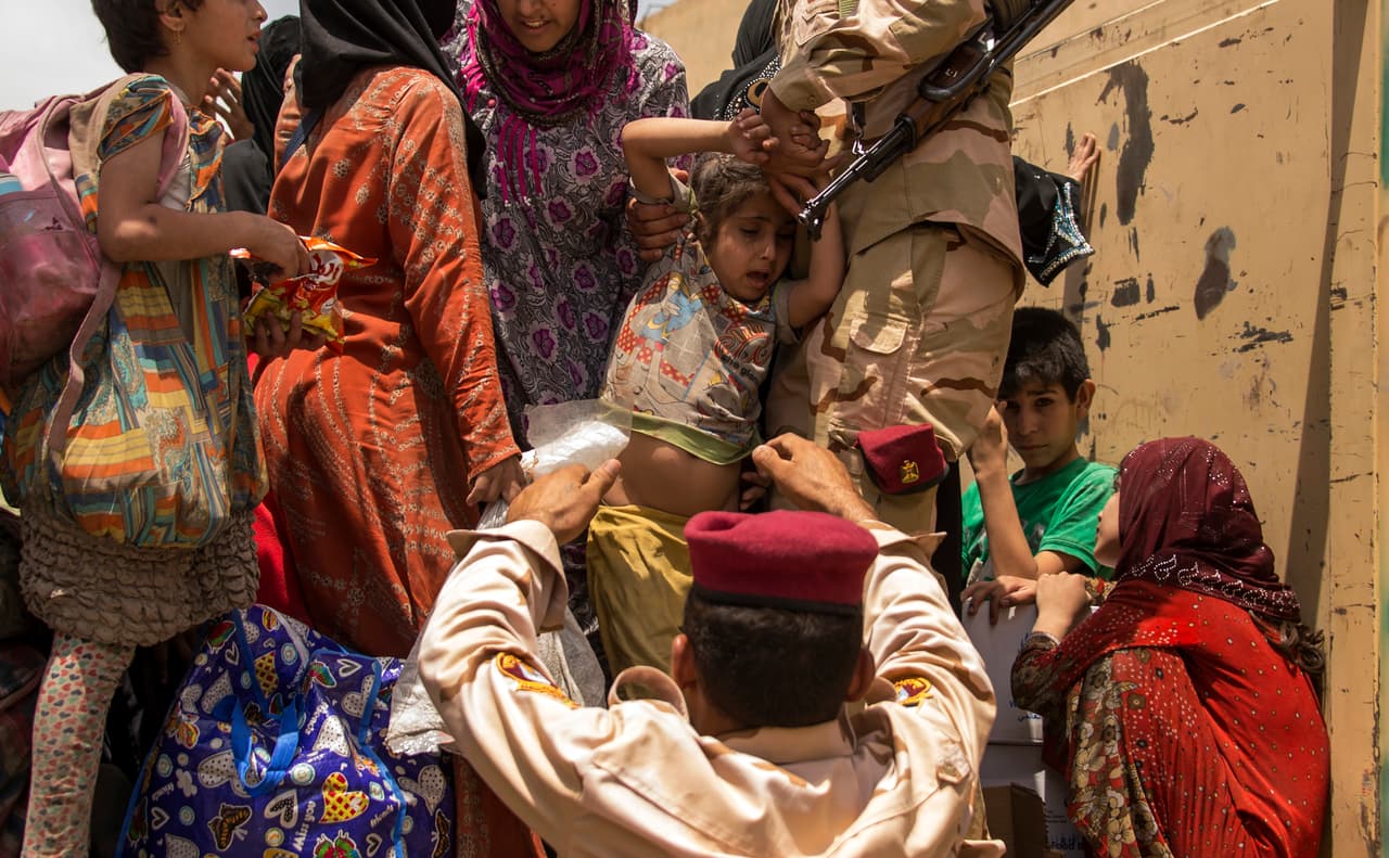 Un miembro de las fuerzas iraquíes ayuda a llevar a una niña, mientras las mujeres que huyeron de los combates con los yihadistas del grupo islámico (ISIS) en la Ciudad Vieja de Mosul se preparan para trasladarse del distrito industrial occidental de la ciudad el 8 de julio de 2017.