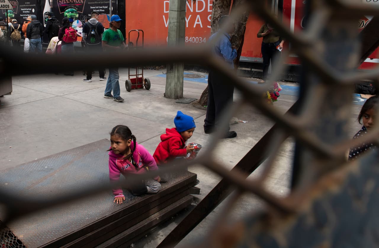 Una pareja de niños juega frente una fila de personas que esperan entrar a Estados Unidos desde Tijuana en el puerto de San Ysidro. 
<br>