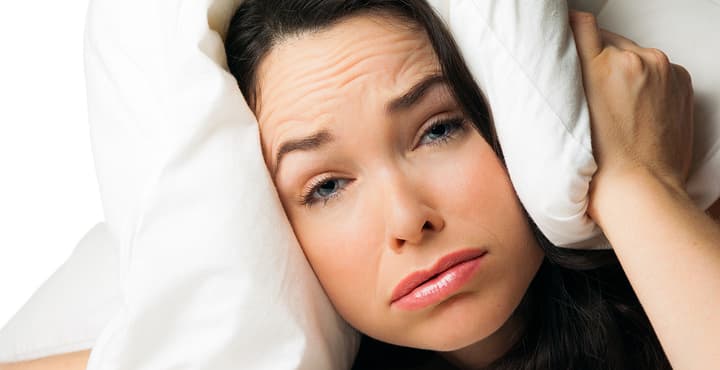 A tired sleepless woman with the pillow over her head . Isolated over white.