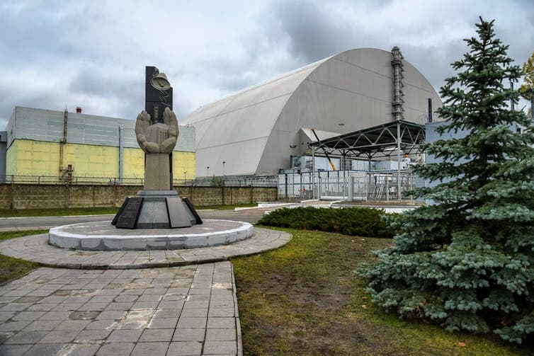 Monumento conmemorativo del desastre de Chernóbil, ubicado ante el reactor, encapsulado en su nuevo escudo de contención.
<br>