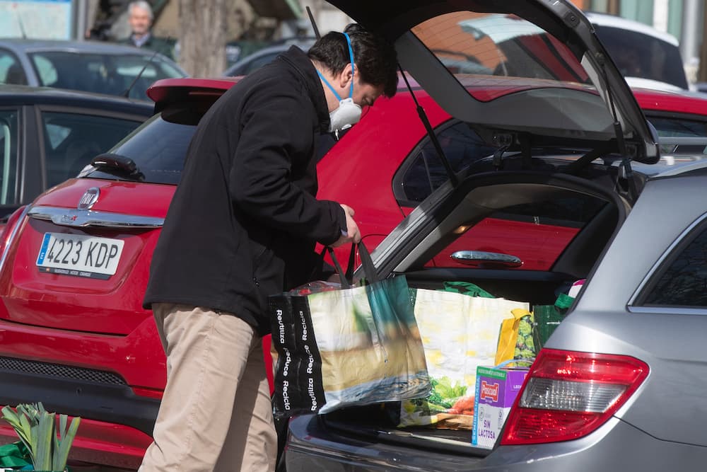 Un hombre que lleva puesta una mascarilla mete las bolsas repretas de la compra en su auto en Madrid la mañana de este martes. Las largas colas en los supermercados en horas de la mañana es algo muy poco usual en la capital española.