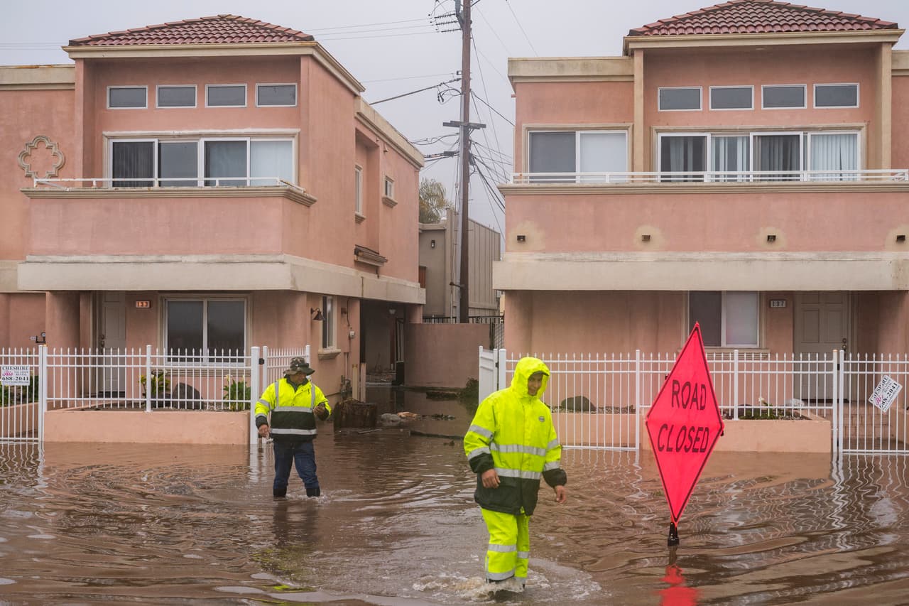 El paso de
<a href="https://www.univision.com/noticias/estados-unidos/california-espera-tormentas-severas-causadas-rios-atmosfericos" target="_blank">las tormentas en California</a> ha dejado al menos 14 muertos y ha obligado la evacuación de comunidades enteras. Al menos 95,000 personas continuaban sin energía eléctrica en la noche de este lunes, según el sitio poweroutage.us. En la imagen, equipos de limpieza caminan en el barrio Rio Del Mar en Aptos, California.