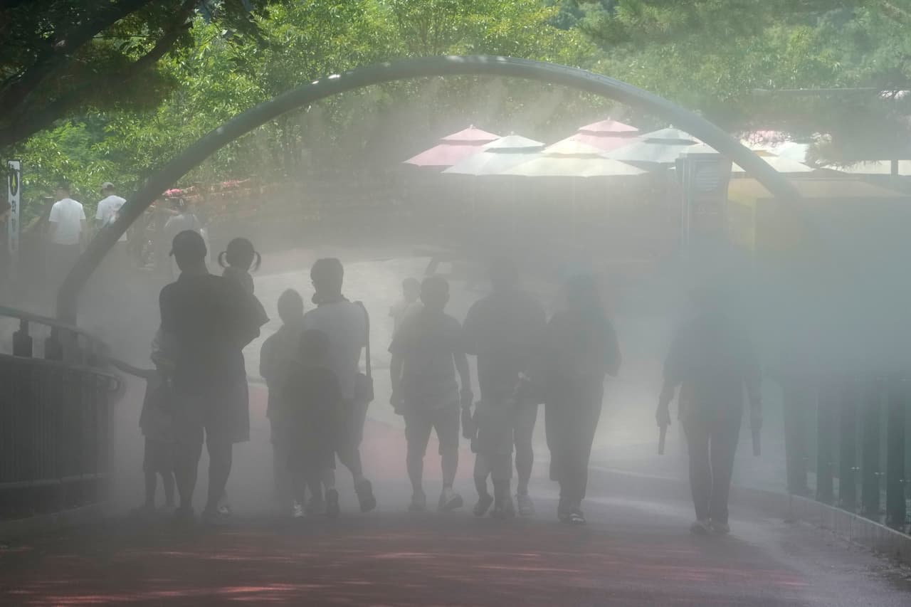 Unos visitantes pasan junto al dispositivo de nebulización refrescante en el sitio turístico de la cueva de Gwangmyeong, en Gwangmyeong, Corea del Sur, el jueves 6 de agosto de 2026.
