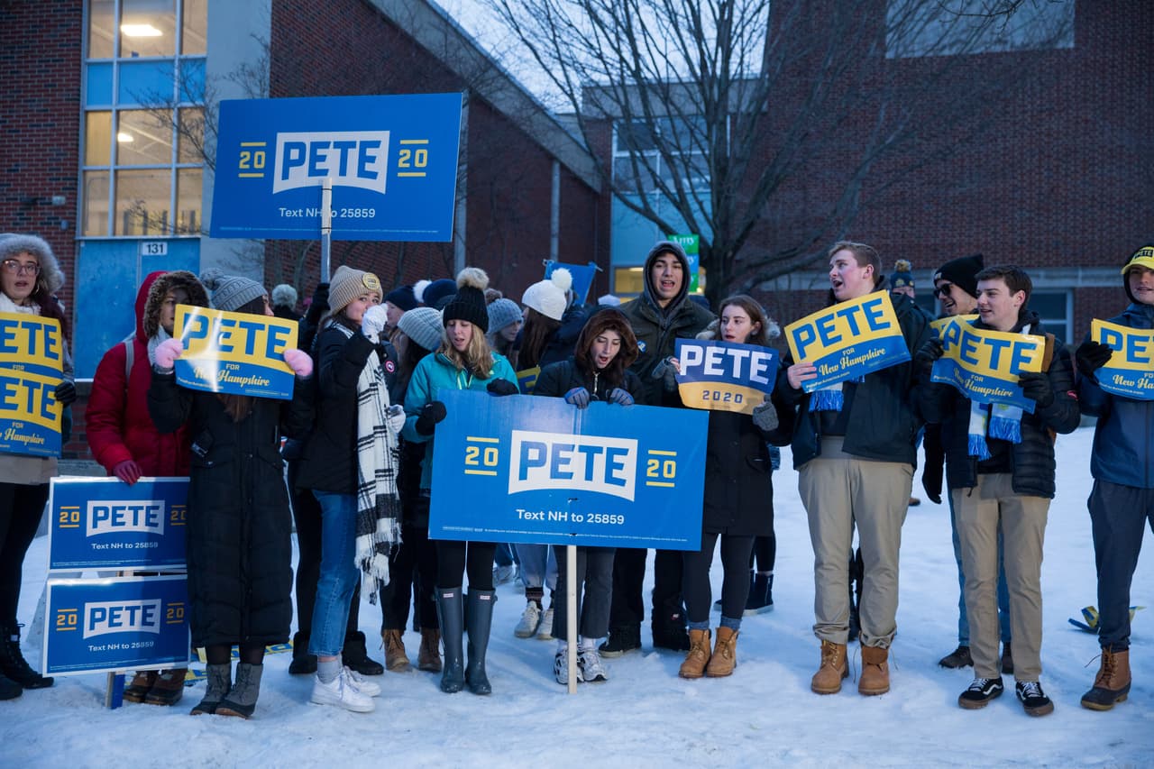 Partidarios del candidato Pete Buttigieg muestran carteles de campaña sobre la nieve frente a una mesa electoral en una escuela de Manchester, New Hampshire. Los demócratas esperan que las primarias en en ese estado definan mejor las preferencias de los demócratas, lugos de las dudas que dejó el caucus de Iowa.