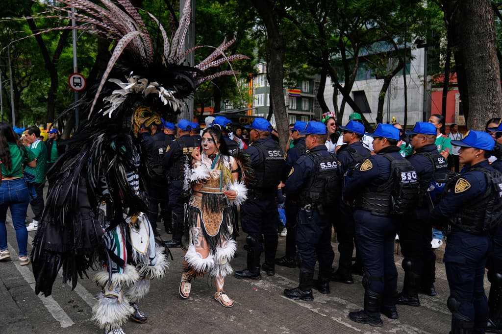 Aficionados al fútbol vestidos como danzantes aztecas pasan junto a una fila de policías