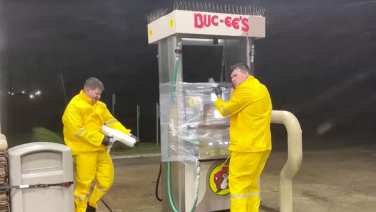 Trabajadores de una gasolinera Bucee's intentan cubrir las mangueras del dispensador para evitar que se dañen con los fuertes vientos.