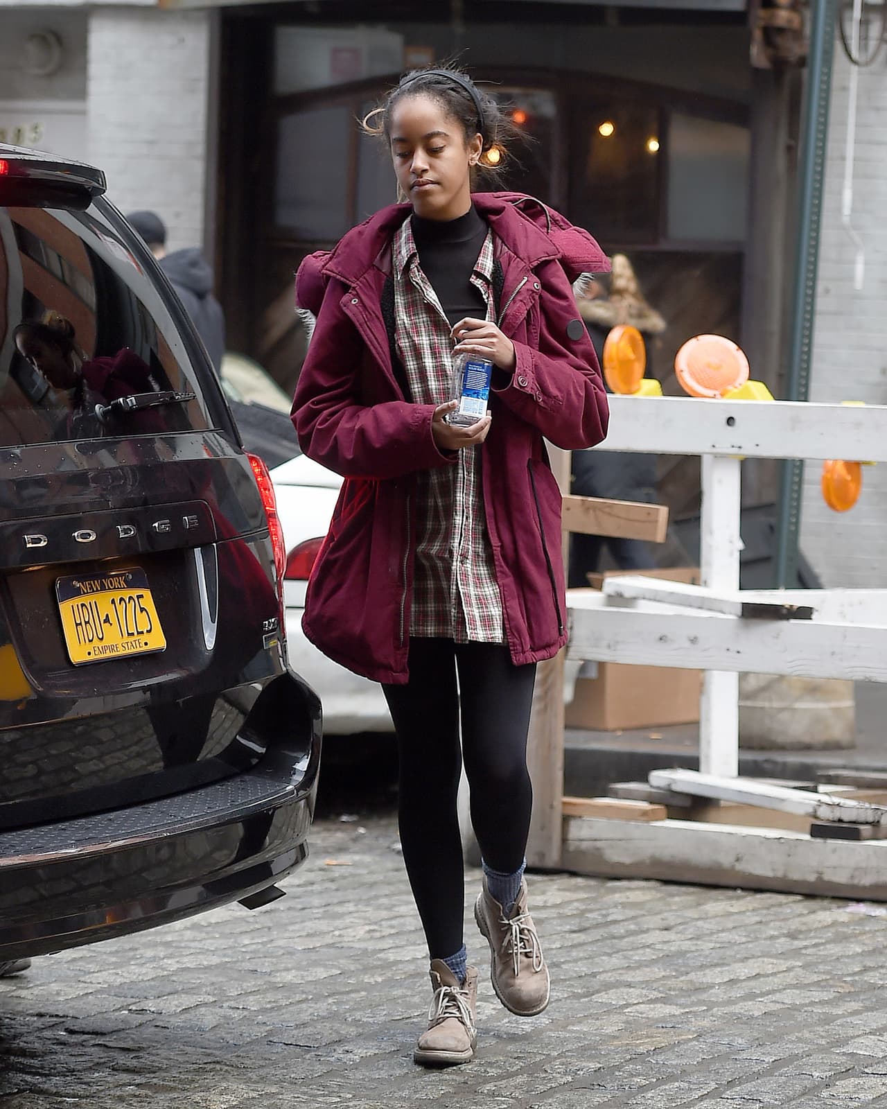 Malia Obama, un poco cansada de los paparazzis, luce un abrigo marrón, camisa a cuadros y su pelo cogido.