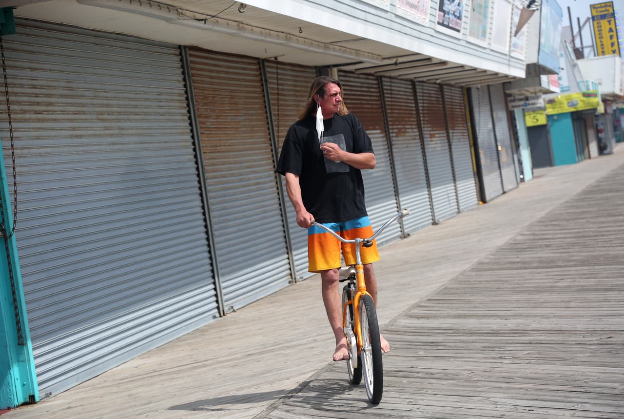 Un hombre se ajusta la máscara mientras conduce su bicicleta por el paseo marítimo.