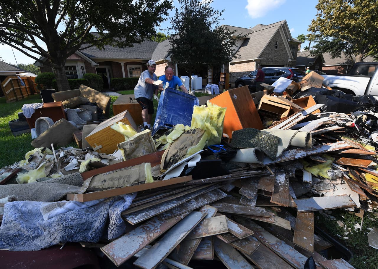 Una pila de objetos dañados, alfombras y pedazos de la estructura se acumulan al frente de una casa que comienza a ser reconstruida en Houston.