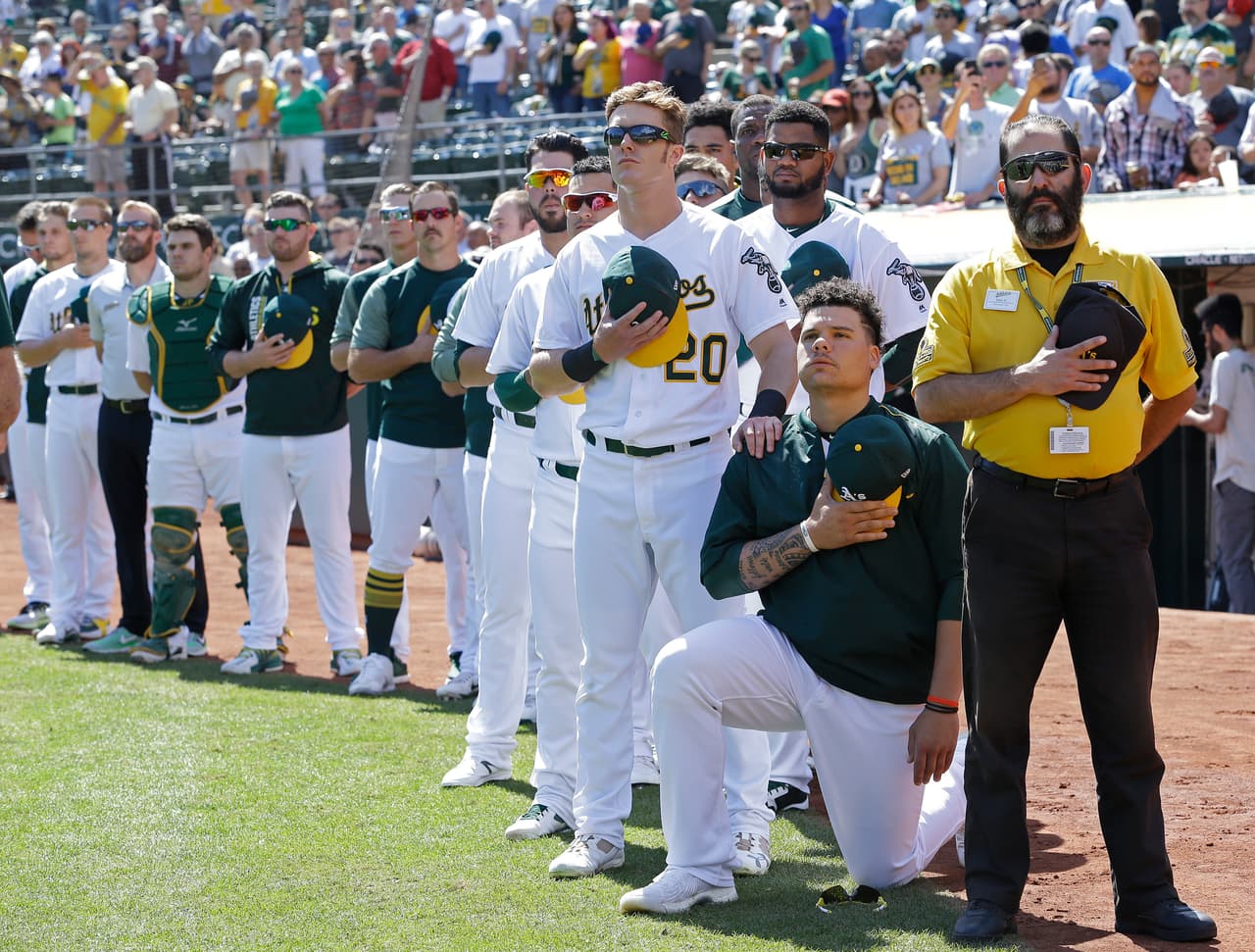 Bruce Maxwell, de los Oakland Athletics, se hinca durante el himno y Mark Canha le muestra su solidaridad con la mano en el hombro.