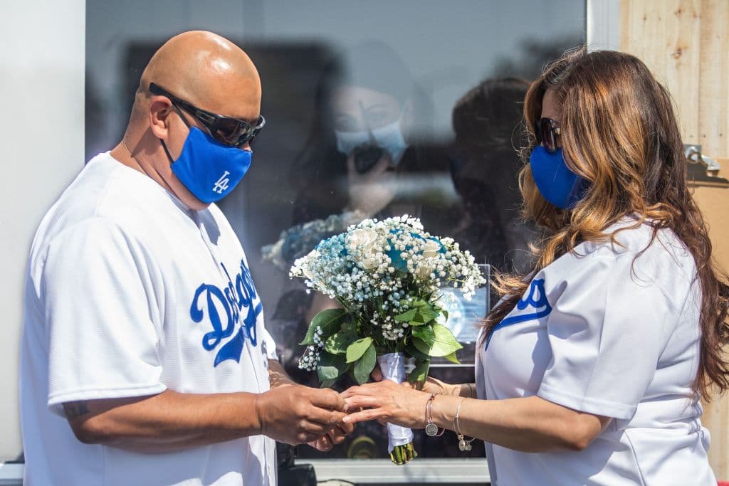 <b>¡Home run!</b> Estos fans de los Dodgers de Los Ángeles llevaron su pasión hasta el 'altar'. Philip Hernández (izq.) le pone el anillo a su novia Marcela Perú, mientras la Secretaria Registradora Erika Patronas (C) observa durante su ceremonia de boda efectuada el 21 de abril de 2020 en Anaheim. Un matrimonio en Califonia dura en promedio 18.2 años, según datos de 2012 del sitio Live Stories y la tendencia desde 2010 es que cada vez duran un poco más.
