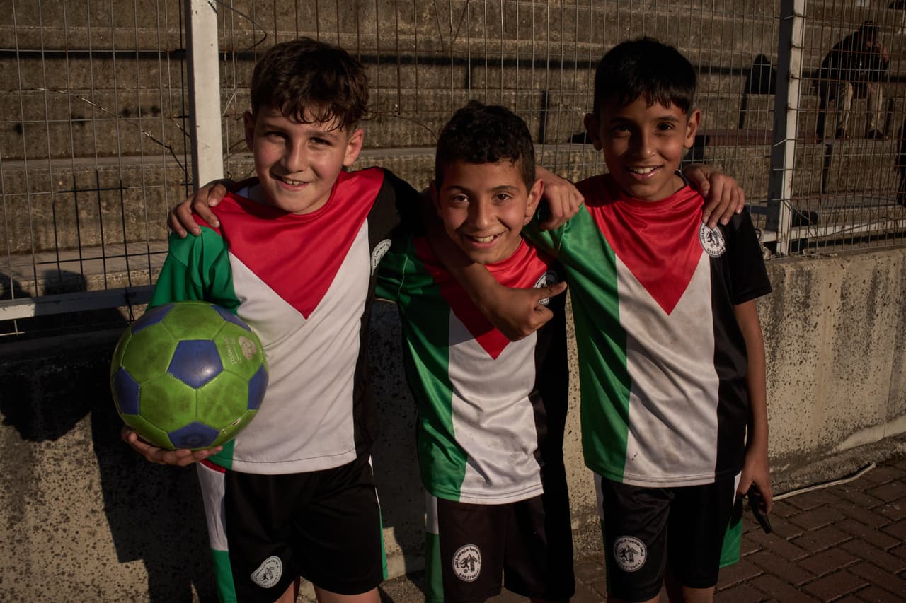 Con camisetas con los colores de la bandera palestina, unos niños sonríen mientras posan tras participar en una sesión de entrenamiento de fútbol en el estadio municipal de Nablus, ciudad de Cisjordania, el jueves 7 de mayo de 2026. (Foto AP/Leo Correa)