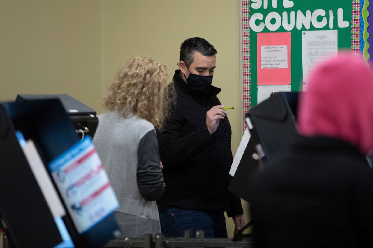 Un trabajador electoral observa si Julio Carreras, en el centro, puede emitir su voto en las elecciones de segunda vuelta del senado de Georgia en la única máquina que funciona después de experimentar problemas en un sitio de votación dentro de un centro para personas mayores, este martes 5 de enero de 2021 en Acworth, Georgia.