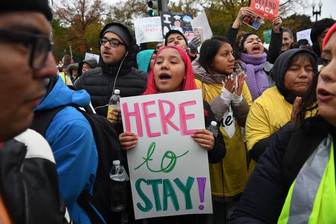 “Aquí para quedarse”, se lee en la pancarta de la manifestante. Los tribunales inferiores dictaminaron que la medida de Trump para rescindir DACA probablemente fue "arbitraria y caprichosa" y violó la Ley de Procedimiento Administrativo.