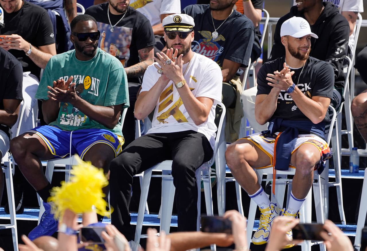 Desde la izquierda, Draymond Green, Klay Thompson y Stephen Curry de los Golden State Warriors aplauden en el escenario antes del inicio del desfile por el campeonato de la NBA en San Francisco, el lunes 20 de junio de 2022. (Foto AP/Eric Risberg)
