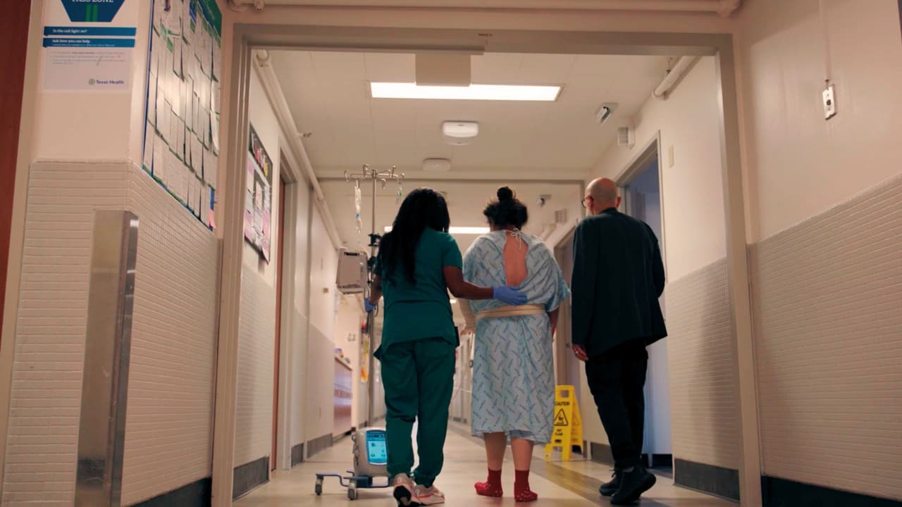 Ernesto Díaz acompaña a una paciente hispana que necesita su ayuda para comunicarse. Caminan por el pasillo de un hospital en Texas junto a una enfermera.